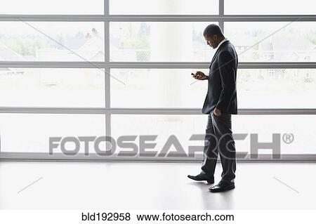 Stock Photo - African businessman text messaging on cell phone. Fotosearch