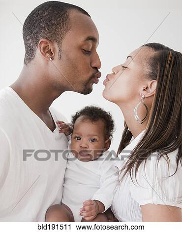 Stock Image - African couple holding baby and kissing. Fotosearch