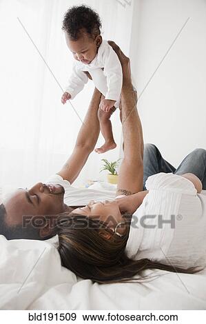 Stock Photo - African couple holding baby up in bed. Fotosearch