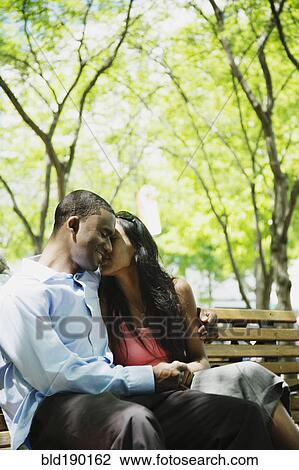 Stock Image - African couple hugging on bench. Fotosearch