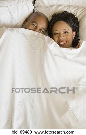 Stock Image - African couple in bed under blanket. Fotosearch