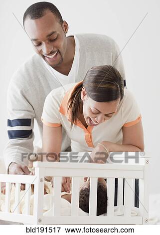 Stock Photo - African couple looking at baby in crib. Fotosearch