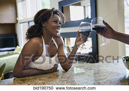 Stock Image - African couple toasting with red wine in kitchen. Fotosearch
