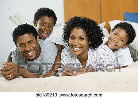 Stock Image - African family laying on bed together. Fotosearch