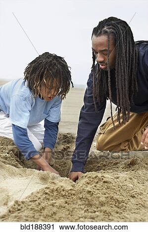 Stock Image - African father and son digging in sand. Fotosearch