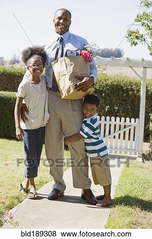 Stock Photo - African father with groceries hugging children. Fotosearch
