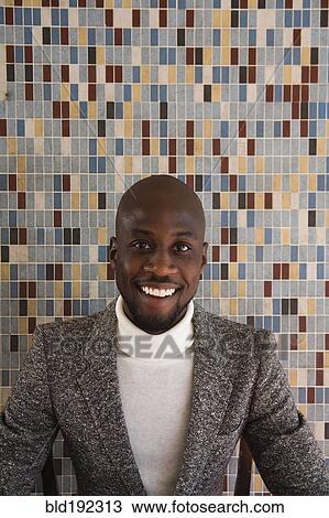 Stock Image - African man in tweed jacket smiling in front of tiled wall. Fotosearch