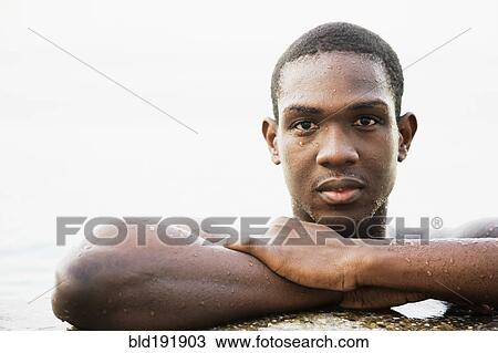 Stock Image - African man leaning on edge of swimming pool. Fotosearch