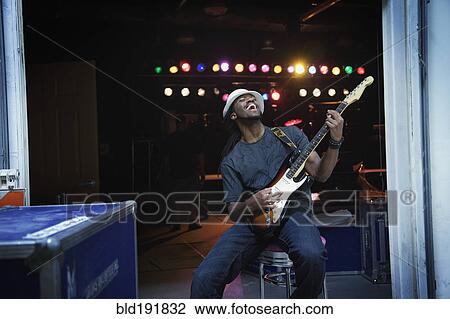 Stock Image - African man playing electric guitar backstage. Fotosearch