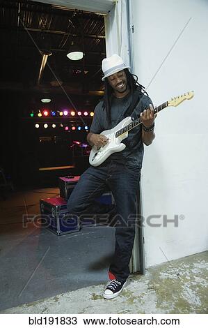 Stock Image - African man playing electric guitar backstage. Fotosearch
