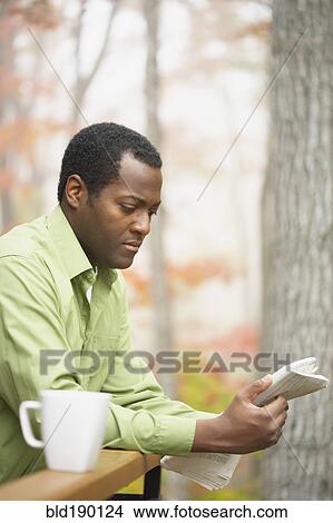 Picture - African man reading newspaper outdoors. Fotosearch