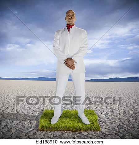 Stock Image - African man standing on patch of grass in desert. Fotosearch