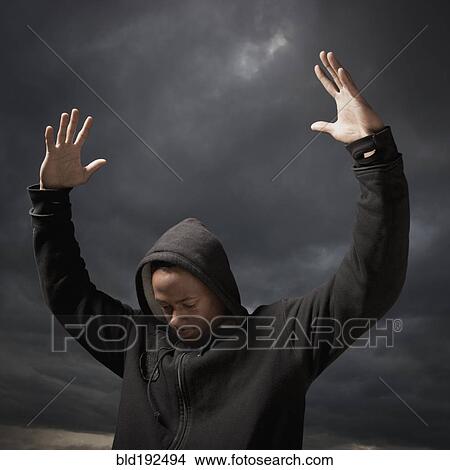 Picture - African man with arms raised, storm clouds in distance. Fotosearch