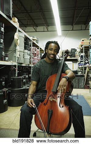 Stock Photo - African man with cello in warehouse. Fotosearch