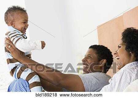 Stock Photo - African parents playing with son in bed. Fotosearch