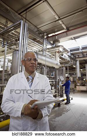Stock Photo - African scientist standing in factory with clipboard. Fotosearch