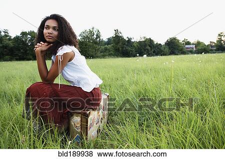 Stock Photo - African woman sitting on suitcase in meadow. Fotosearch
