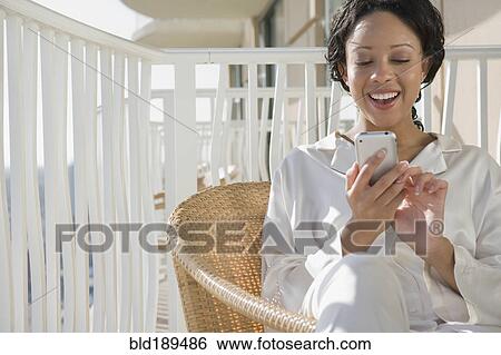 Stock Photograph - African woman using cell phone on balcony. Fotosearch