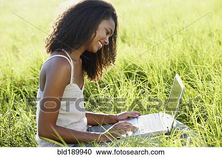Stock Image - African woman using laptop in meadow. Fotosearch