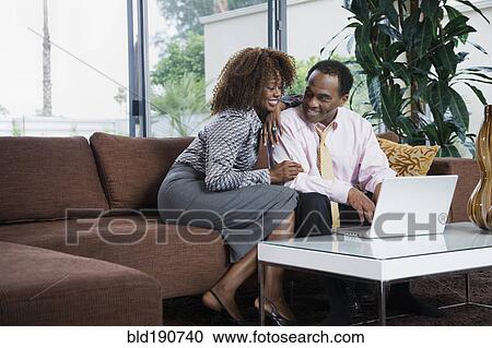 Stock Image - African woman watching husband type on laptop in living room. Fotosearch