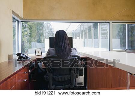 Stock Image - Asian businesswoman sitting at desk. Fotosearch
