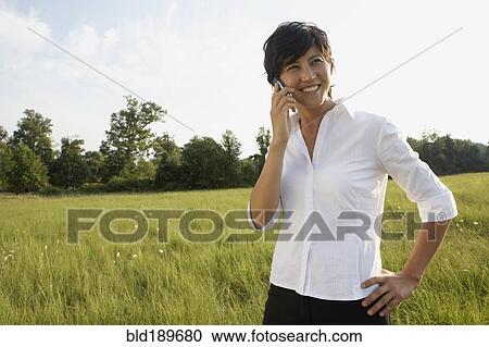 Stock Image - Asian businesswoman talking on cell phone in field. Fotosearch