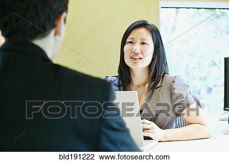 Stock Image - Asian businesswoman talking to co-worker. Fotosearch