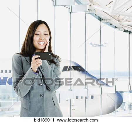 Stock Image - Asian businesswoman text messaging in airport. Fotosearch