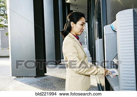 Picture - Asian businesswoman using ATM outdoors. Fotosearch