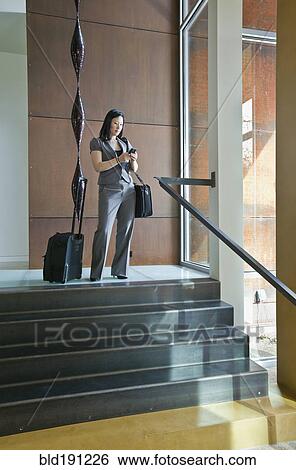 Stock Photograph - Asian businesswoman with suitcases looking at cell phone. Fotosearch