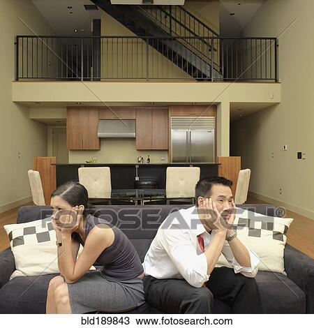 Stock Image - Asian couple ignoring each other on sofa. Fotosearch