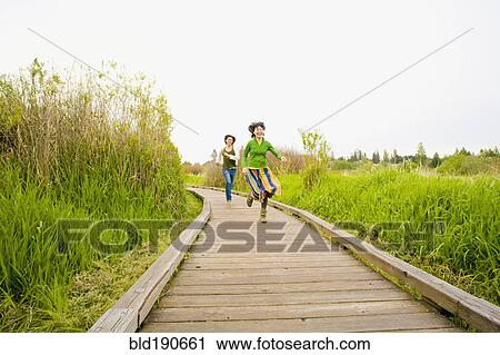 Stock Image - Asian couple running on wooden path. Fotosearch