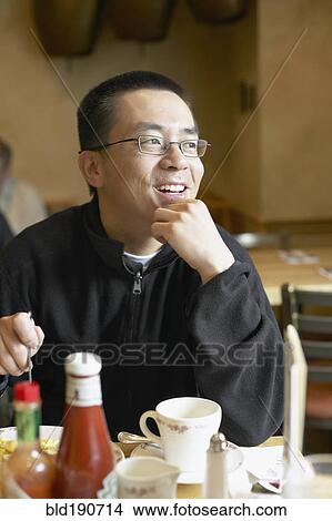 Picture - Asian man eating in restaurant. Fotosearch