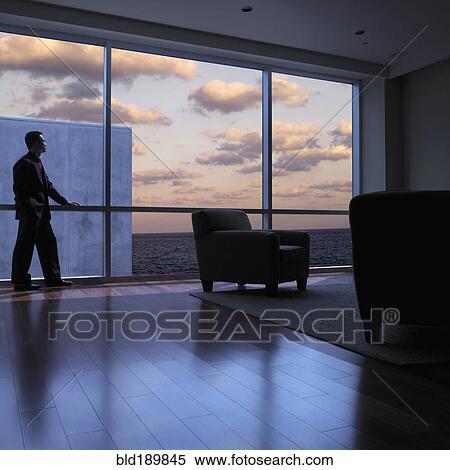 Stock Photography - Asian man looking out window at dusk. Fotosearch