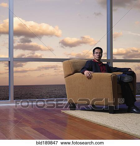 Stock Photo - Asian man sitting next to window overlooking water. Fotosearch