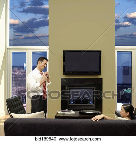 Stock Image - Asian man taking off tie and looking at wife. Fotosearch