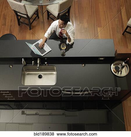 Asian man typing on laptop in kitchen View Large Photo Image Stock Photo - Asian man typing on laptop in kitchen. Fotosearch