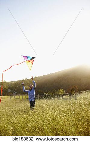Stock Image - Asian woman flying kite in field. Fotosearch