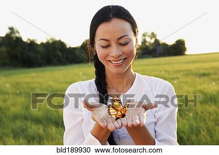 Stock Image - Asian woman holding butterfly in hands. Fotosearch