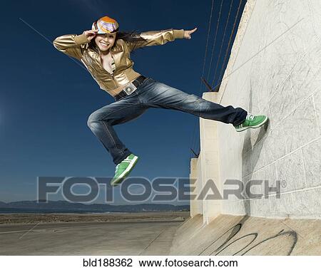 Stock Image - Asian woman jumping off wall. Fotosearch
