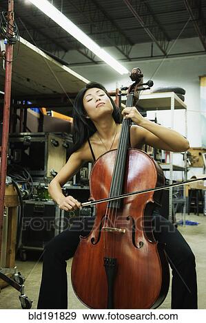 Stock Photo - Asian woman playing cello in warehouse. Fotosearch
