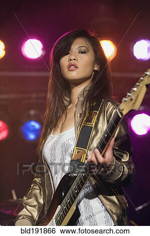 Stock Photograph - Asian woman playing electric guitar onstage. Fotosearch