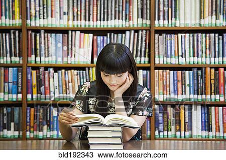 Stock Image - Asian woman reading book in library. Fotosearch