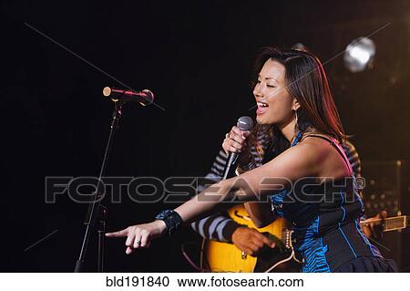 Stock Image - Asian woman singing and pointing onstage. Fotosearch