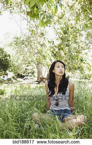 Stock Photo - Asian woman sitting cross-legged in grass. Fotosearch