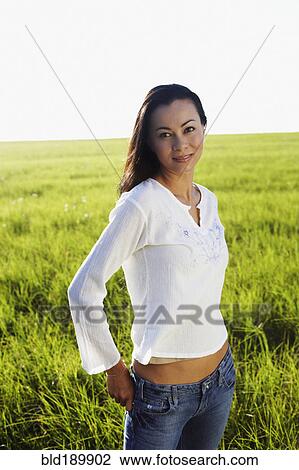 Stock Image - Asian woman standing in meadow with hands in pockets. Fotosearch