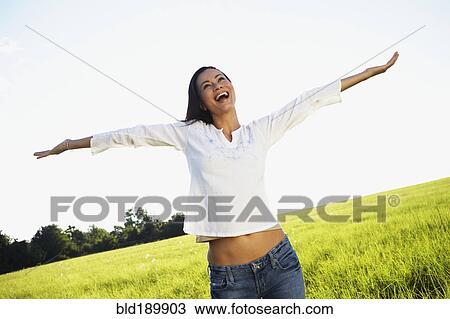 Stock Image - Asian woman standing in meadow with arms outstretched. Fotosearch