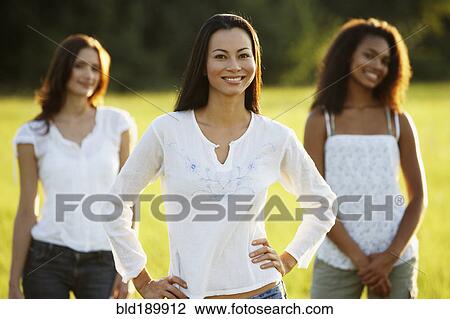 Stock Image - Asian woman standing in meadow with friends in the background. Fotosearch