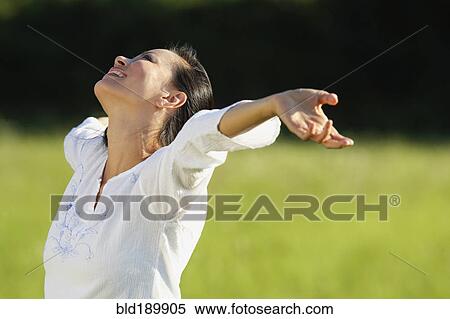 Stock Photography - Asian woman standing in meadow with arms outstretched. Fotosearch