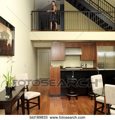 Stock Image - Asian woman standing on second level of loft. Fotosearch